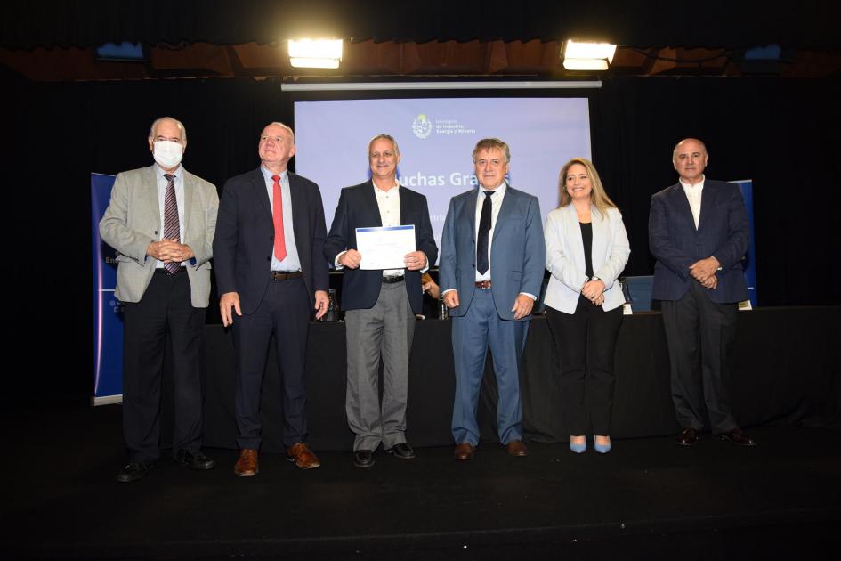 Certificado para Mastergraf SRL Un hombre muestra su certificado junto a las autoridades; detrás, una pantalla azul