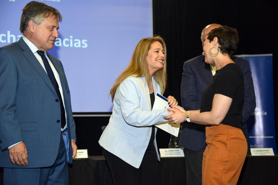 Una mujer saluda a Pecoy al recibir el certificado; al lado de la directora, el ministro