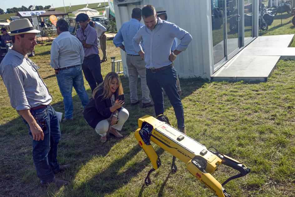 Directora Pecoy se agacha para observar un robot canino; de pie hay otras personas