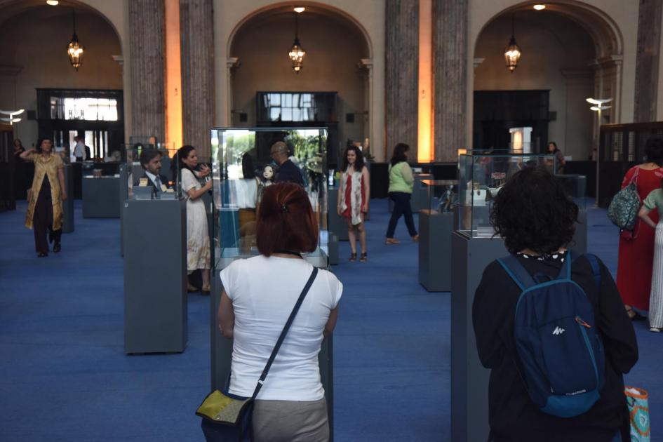 La exposición puede visitarse en el hall del BROU casa central, de 13.00 a 18.00 horas Personas, de edspalda, miran los premios; detrás se ven detalles del hall del BROU Central