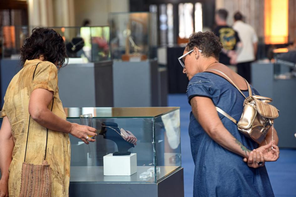 Dos mujeres observan un collar dentro de una caja de cristal