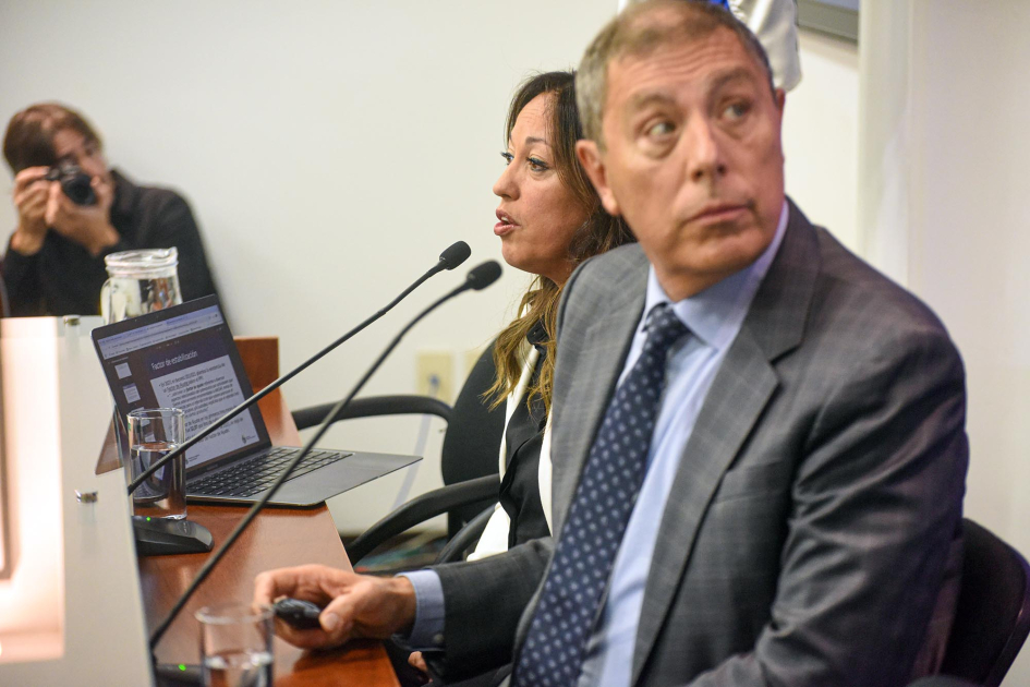 Oddone y Cardona en conferencia de prensa Oddone mira al costado. Cardona habla a micrófono. Al fondo hay un hombre con una cámara de fotos