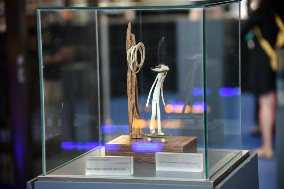 Pieza premiada en la edición 2022 Figura humana abstracta en una patineta junto a objeto en madera, en caja de cristal