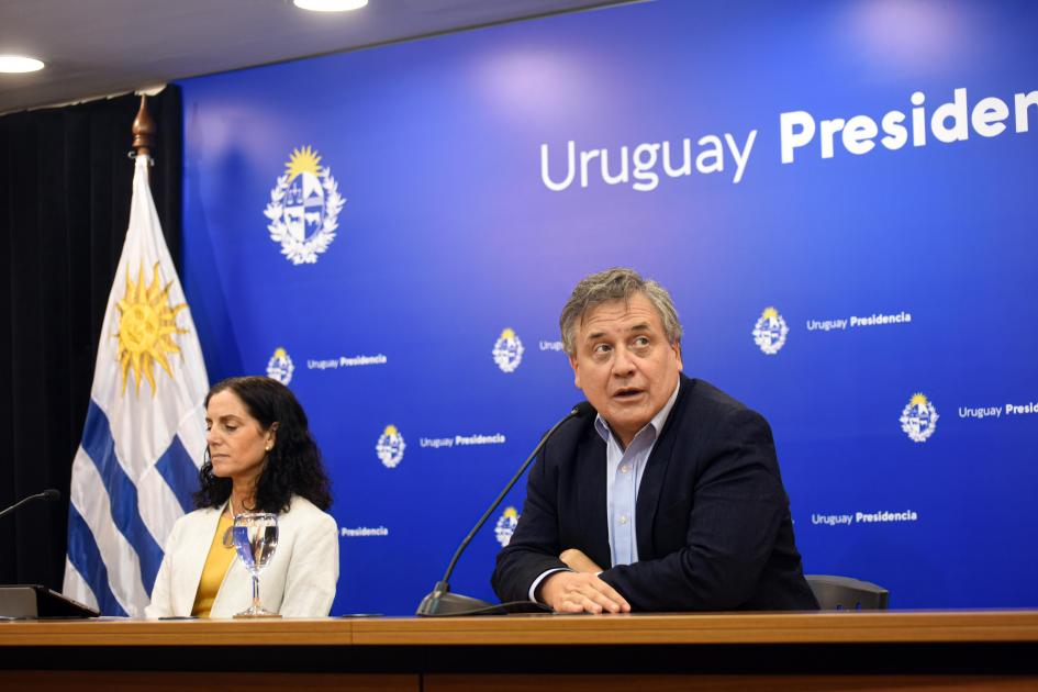 Los ministros Omar Paganini y Azucena Arbeleche estuvieron a cargo de la conferencia de prensa Ministro Paganini junto a ministra Arbeleche; detrás, banner azul de Presidencia; al lado, bandera
