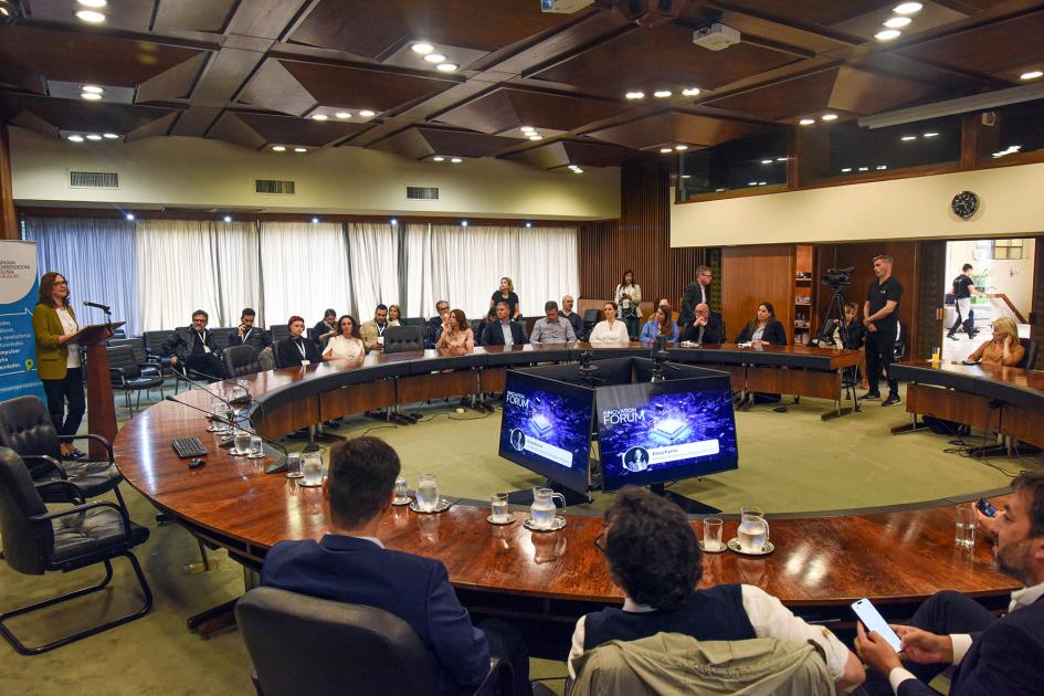 La ministra Elisa Facio abrió la instancia de intercambio Ministra Facio habla desde un atril a un auditorio que integra una mesa redonda y sillas al costado