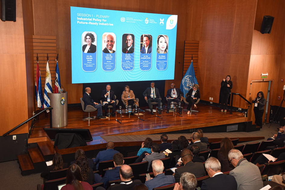 Primer panel de la conferencia, realizado luego de la sesión inaugural Al fondo, escenario con panelistas y pantalla; más cerca, público, de espaldas