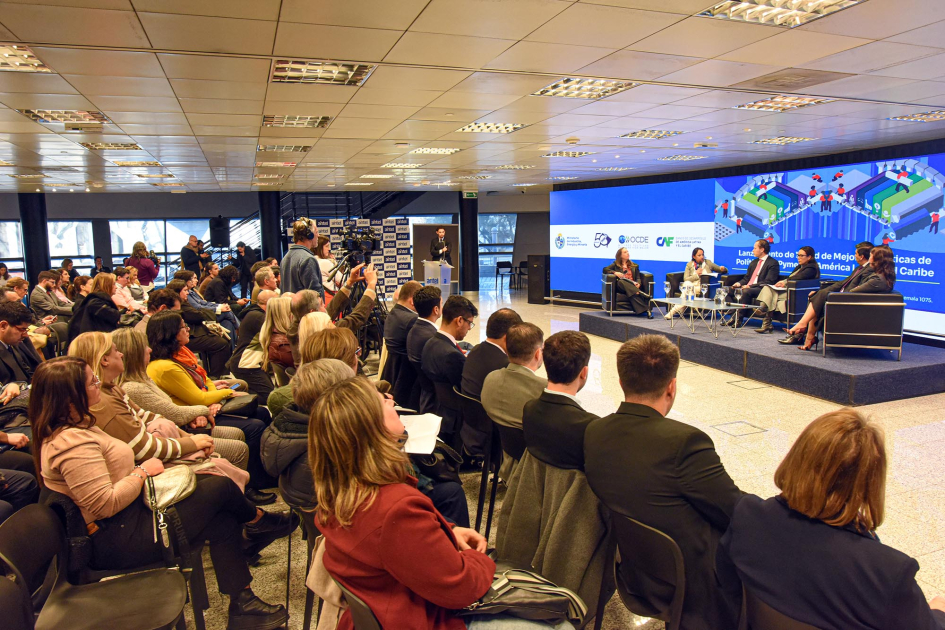 Público, sentado; al fondo, panelistas, sentados