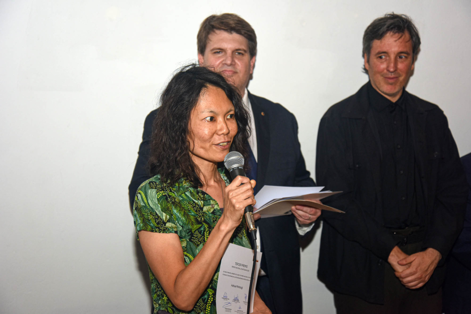 Hatsue Motosugi (tercer premio en Artesanía de producción) Mujer sostiene diploma; detrás, autoridades