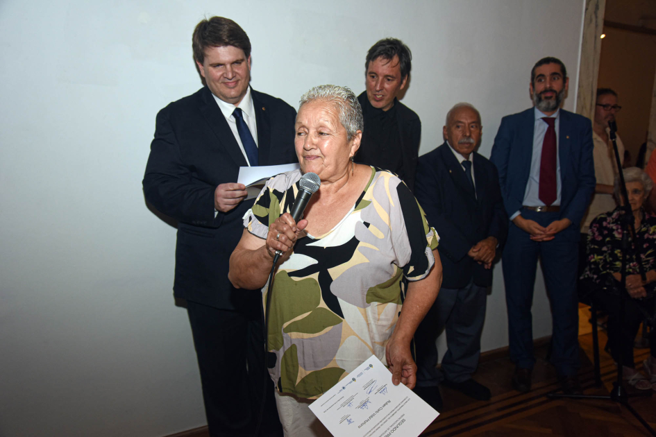 Diploma de Ruben Vidal (segundo premio en Artesanía de producción) Mujer sostiene diploma; detrás, autoridades