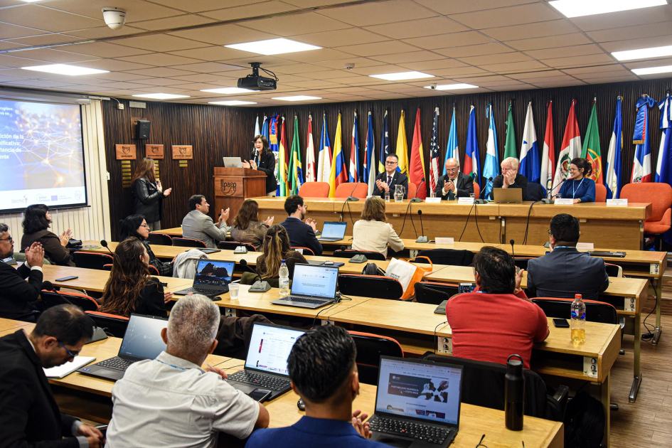 Capacitación sobre estadísticas subnacionales para medir la conectividad universal y significativa Participantes vistos de atrás; al fonod, mesa con autoridades y banderas