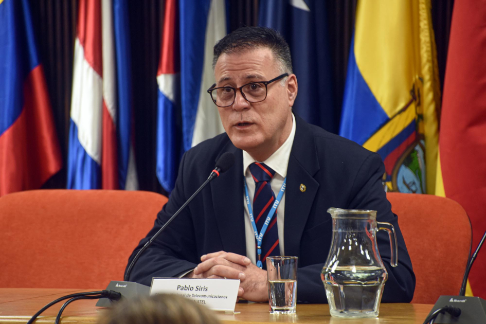 Director de Dinatel, Pablo Siris Siris habla, sentado; detrás, banderas