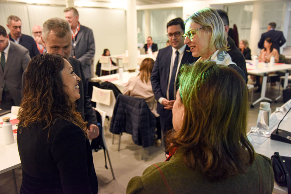 Apertura del encuentro Ministra Cardona dialoga con otros participantes, de pie; más atrás, participantes de pie y en mesas