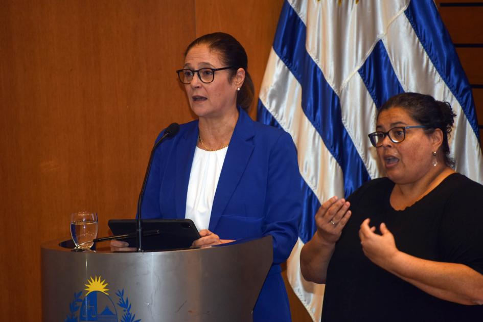 Ministra Elisa Facio Ministra Facio habla desde un atril; al lado, intérprete de lengua de señas; detrás, bandera