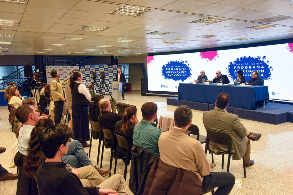 Lanzamiento de la convocatoria del programa Adecuación Tecnológica Al fondo, mesa de autoridades y pantalla con el nombre del programa; más cerca, público