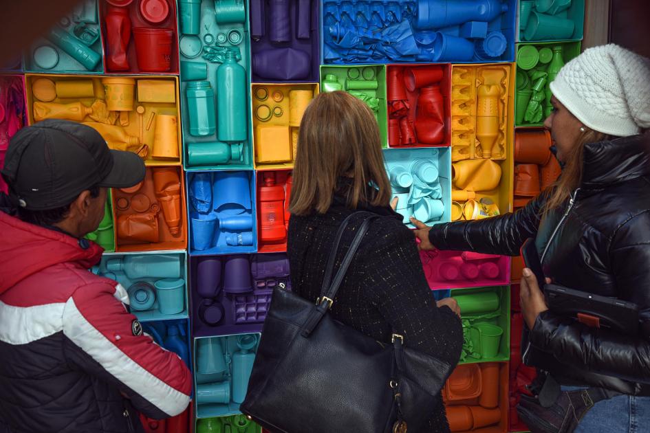 Personas miran una pared realizada con envases de colores