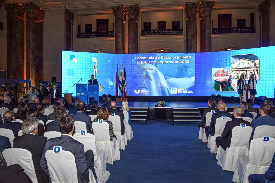 El evento es organizado por el Banco República y la Unión de Exportadores del Uruguay Sala del evento; al fondo, escenario con una pantalla y atril con el maestro de ceremonias