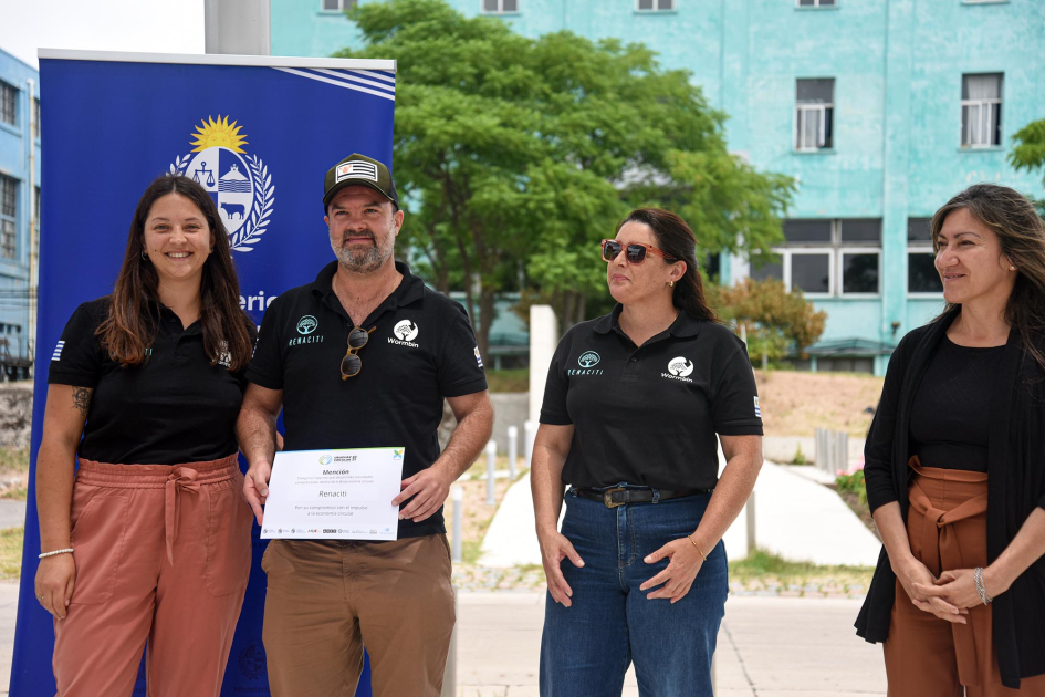 Grupo de personas sonríe; un hombre sostiene un diploma