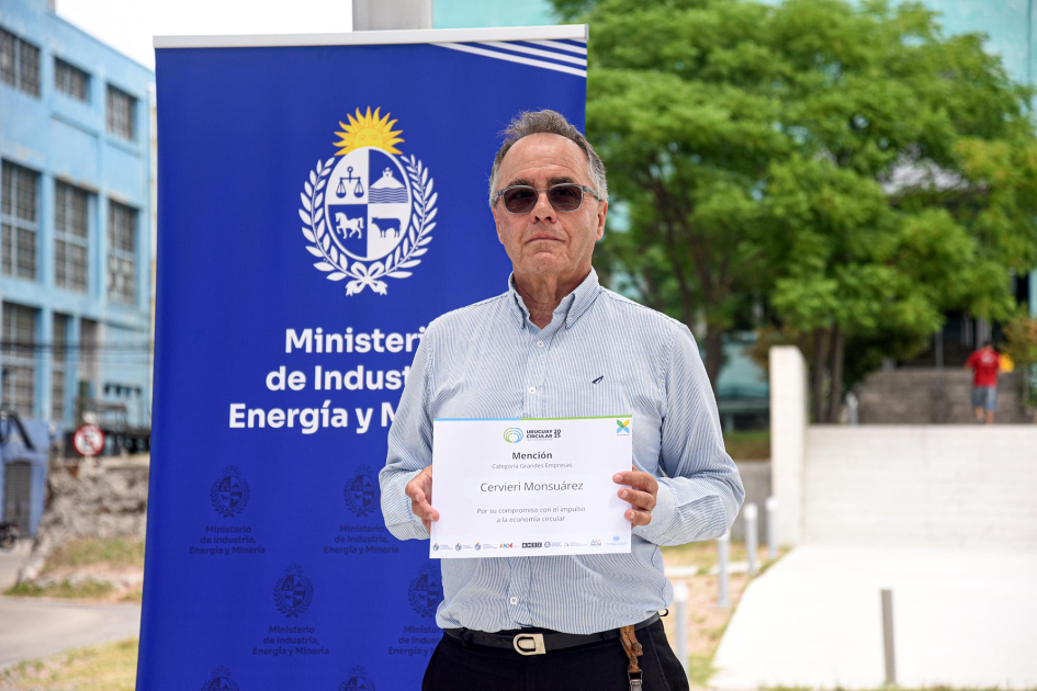Hombre sostiene un diploma al lado de un banner del MIEM