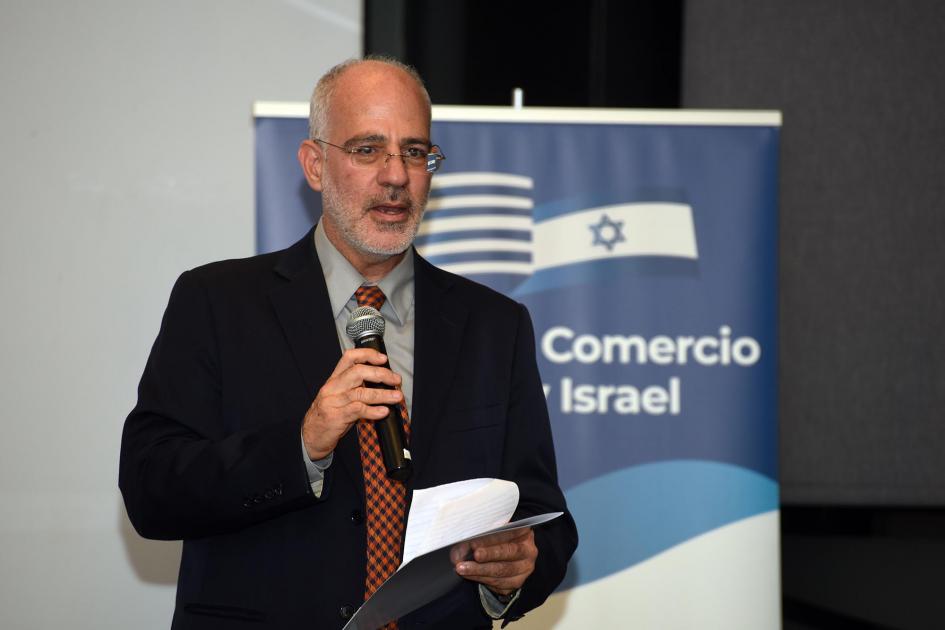 Embajador de Israel en Uruguay, Yoed Magen Embajador de Israel en Uruguay, Yoed Magen, habla con un micrófono; detrás, banner de organizadores