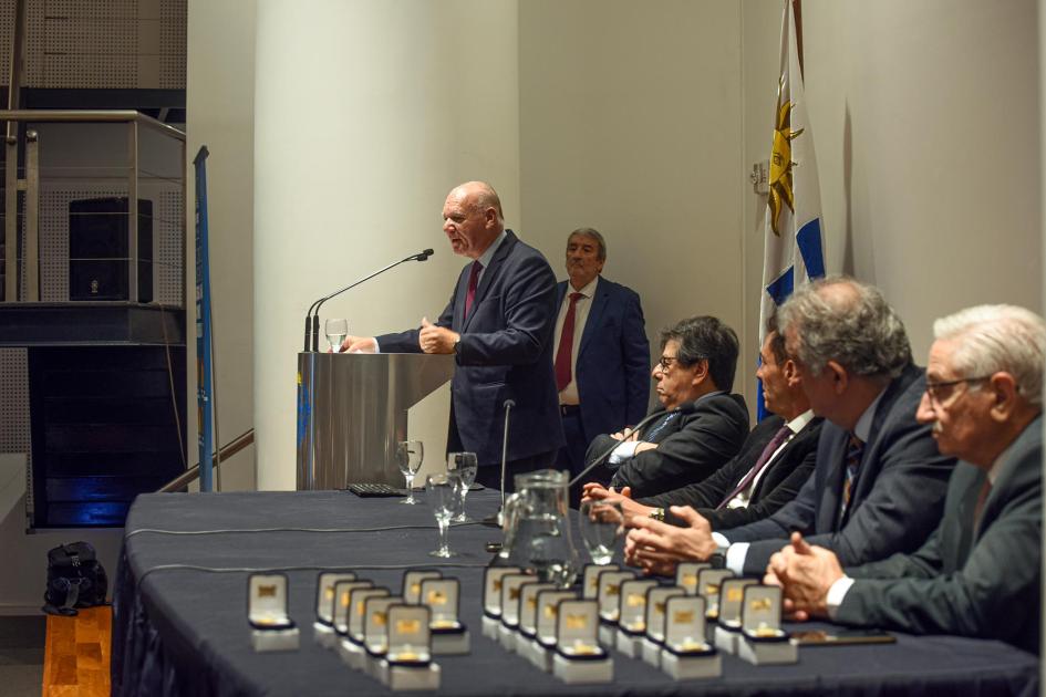A lo lejos, Verri habla desde un atril; detrás, bandera y maestro de ceremonias; más cerca, mesa