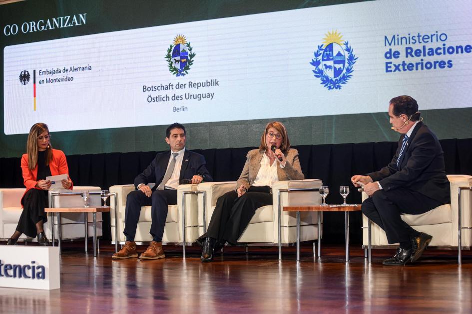 El Gobierno nacional participó del evento con la presencia de varios jerarcas Cuatro personas, dos hombres y dos mujeres, dialogan en sillones; detrás, logos del Gobierno
