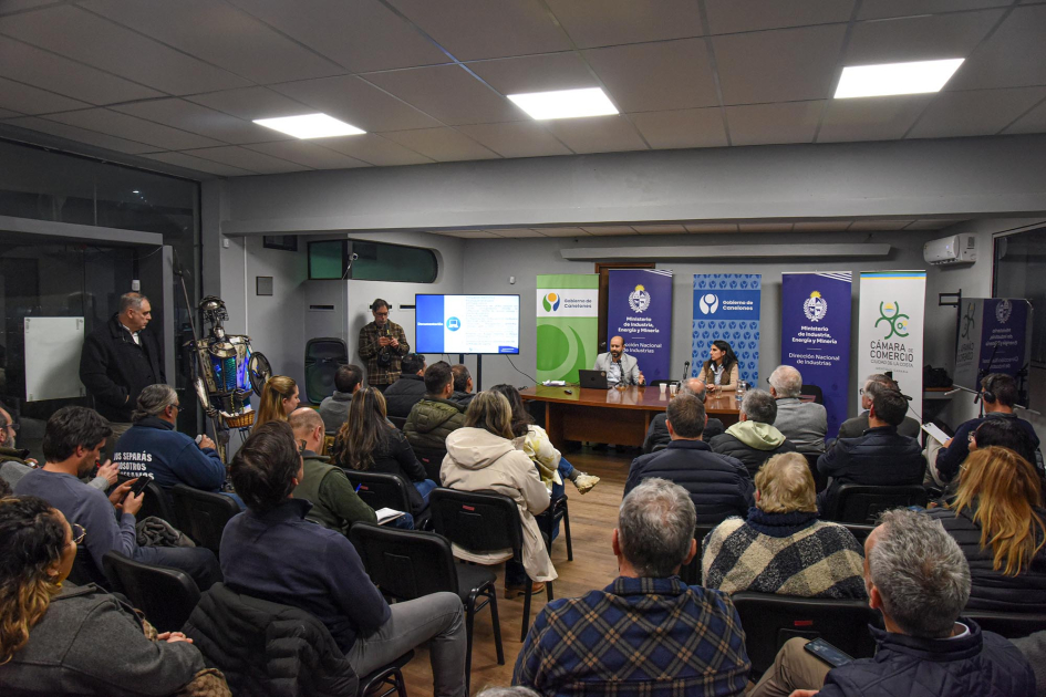 Al fondo, mesa con equipo técnico; más cerca, público, de espaldas