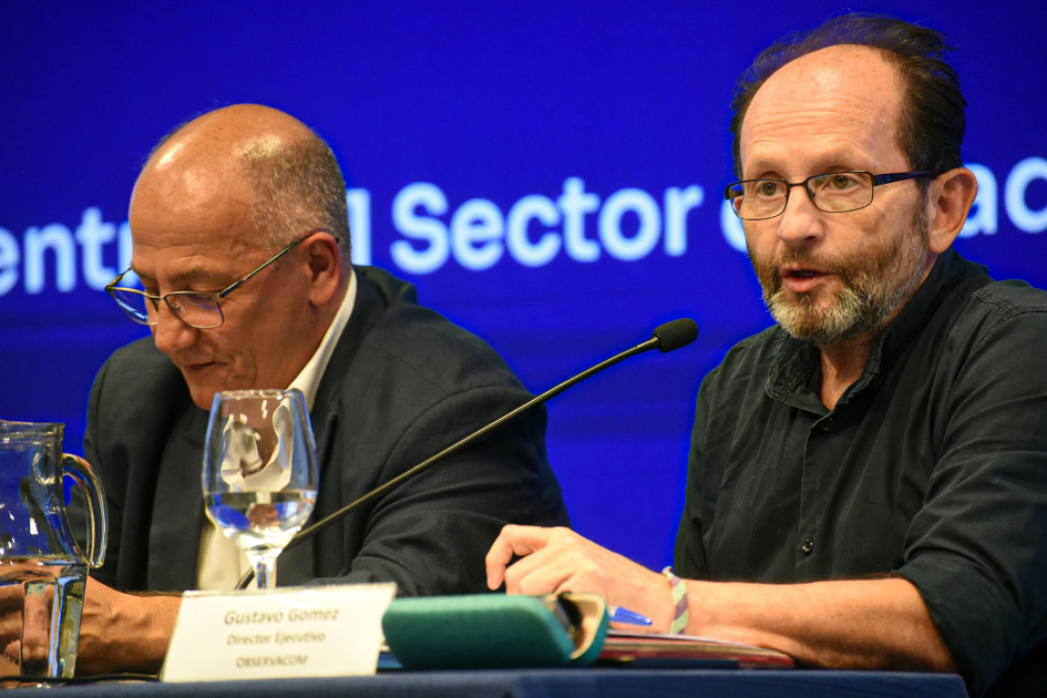 Gonzalo Balseiro y Gustavo Gómez. Detrás, pantalla azul con texto.