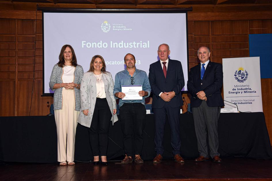 Premio para Juan Ignacio Artola Canclini Autoridades acompañan a un hombre que muestra su diploma; detrás hay una pantalla