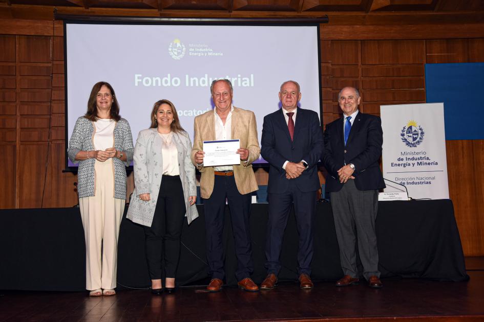 Premio para Olivares Salteños SRL Autoridades acompañan a un hombre que muestra su diploma; detrás hay una pantalla