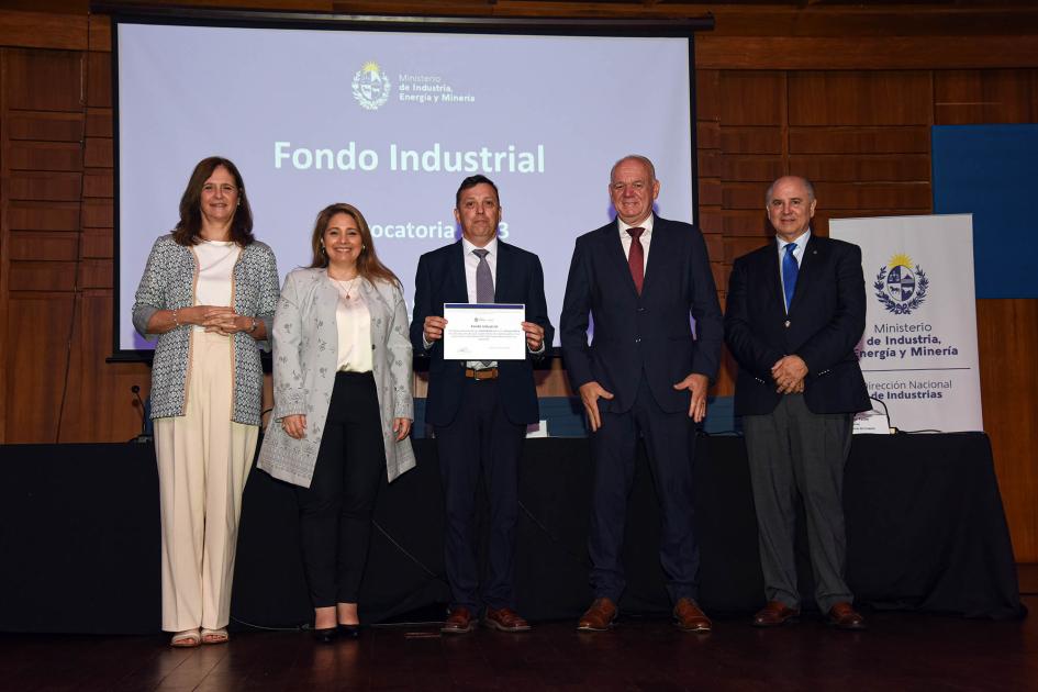 Premio para Neigarsan SA Autoridades acompañan a un hombre que muestra su diploma; detrás hay una pantalla