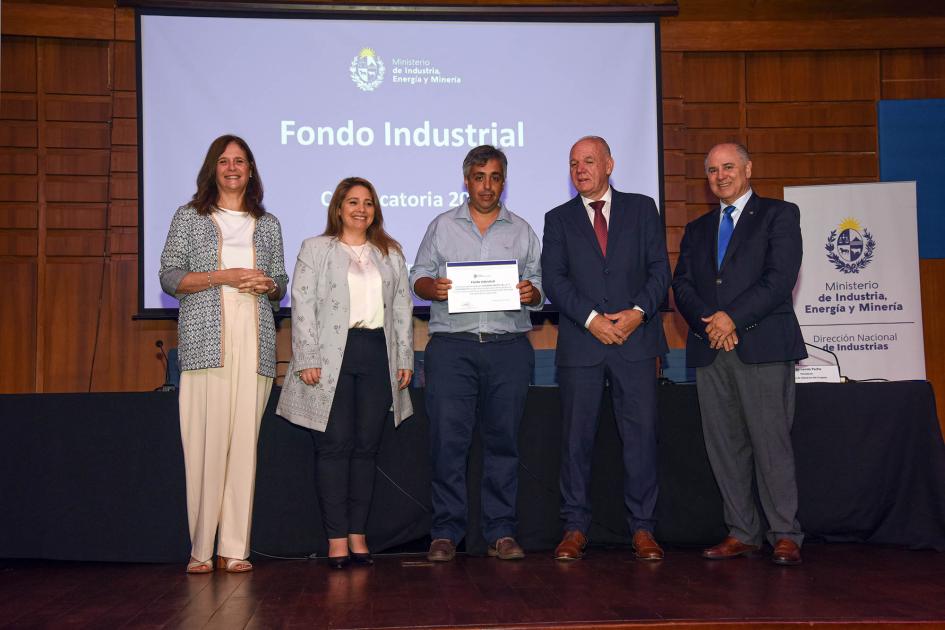Premio para Giovanni Sauto SRL Autoridades acompañan a un hombre que muestra su diploma; detrás hay una pantalla