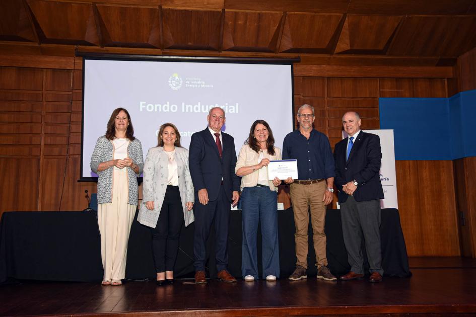 Premio para Eko Varmo SRL Autoridades acompañan a una mujer que muestra su diploma; detrás hay una pantalla