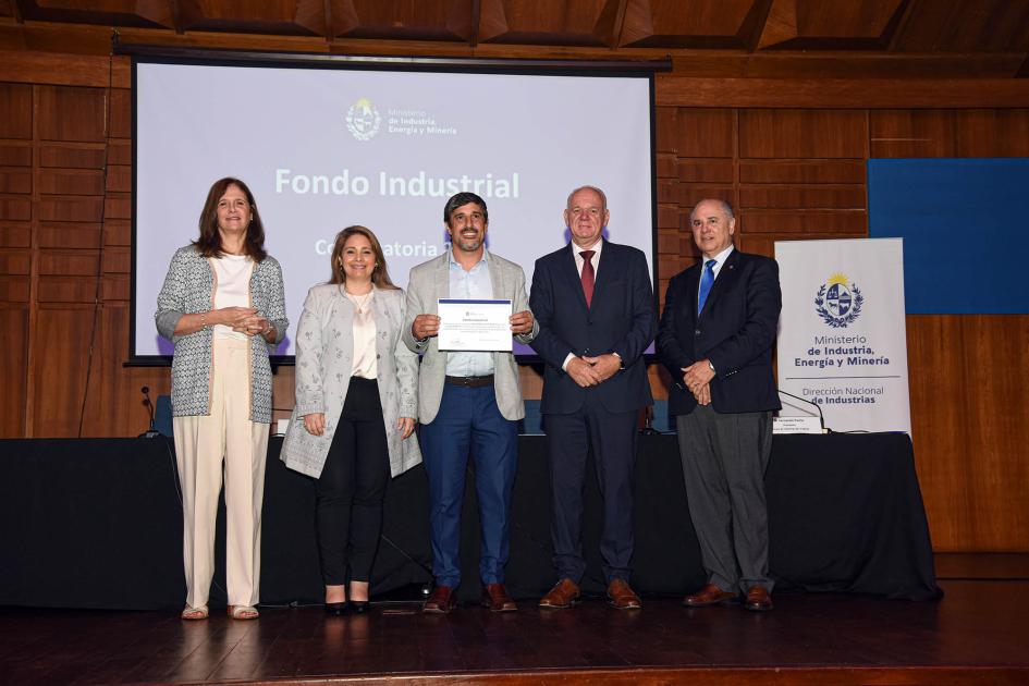 Premio para Maestros Cafeteros SRL (Saint Café) Autoridades acompañan a un hombre que muestra su diploma; detrás hay una pantalla
