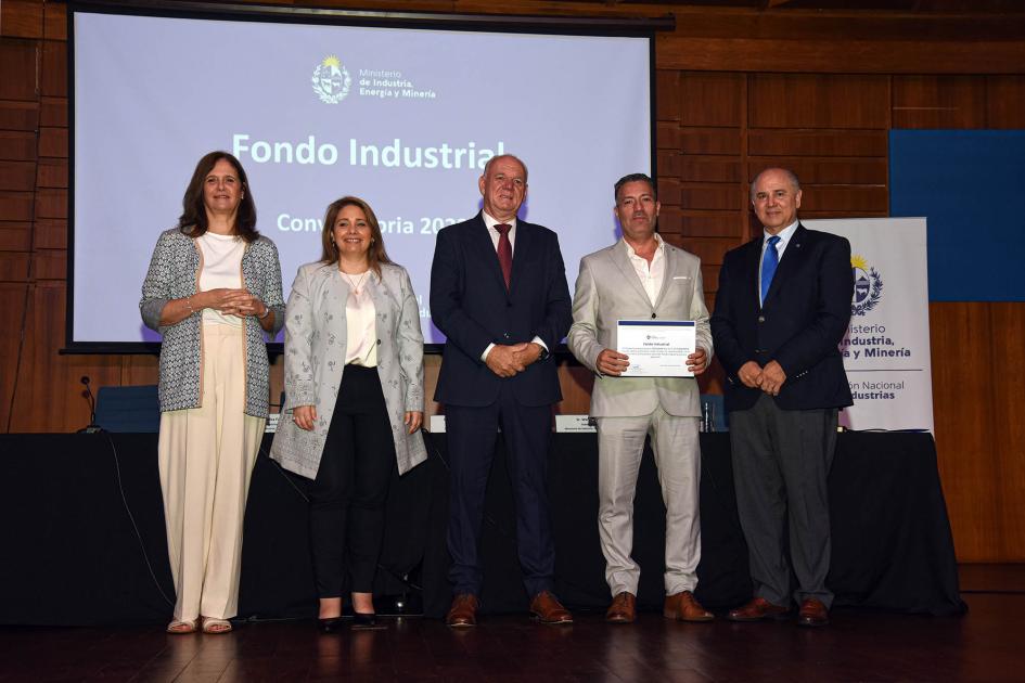 Premio para Sedumar SA Autoridades acompañan a un hombre que muestra su diploma; detrás hay una pantalla