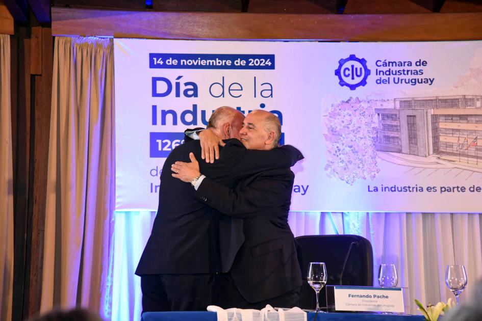 Ministro interino Walter Verri y presidente de la CIU, Fernando Pache Verri abraza a Pache; detrás, pantalla