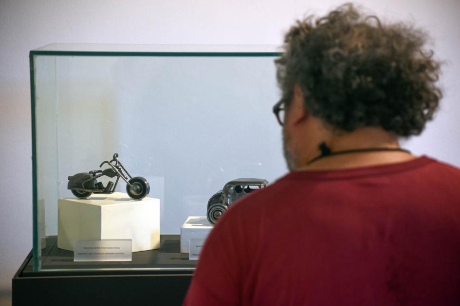 La exhibición puede visitarse hasta marzo de 2025 Una mujer observa artesanías (moto y auto antiguo, de metal)