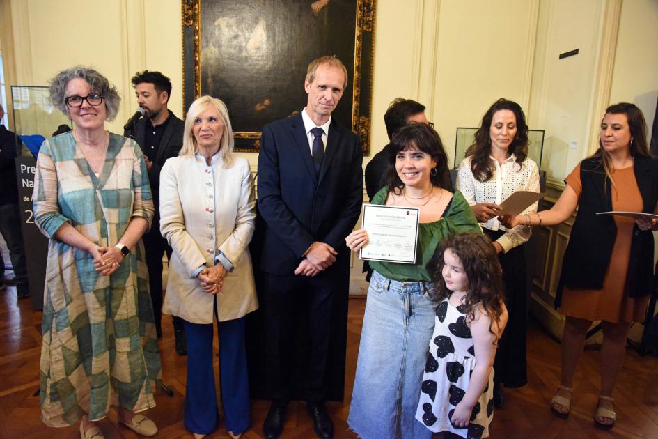 Artesana reconocida en el Premio Nacional de Artesanía 2024 Ganadora muestra diploma junto a autoridades; al lado, una niña