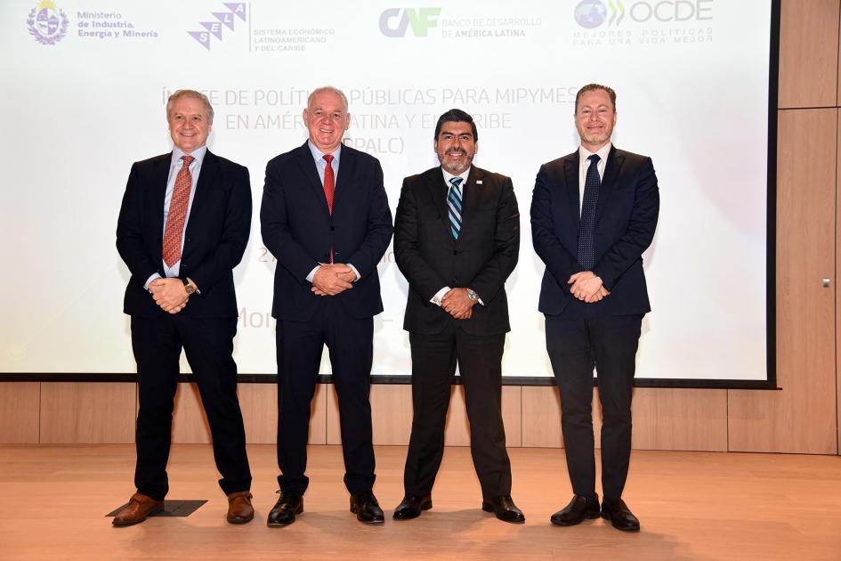 Foto oficial de los expositores Expositores posan en el escenario; detrás, una gran pantalla blanca