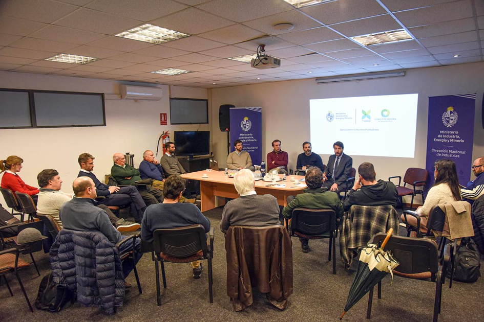 Participantes sentados; al fondo mesa con personas sentadas y pantalla