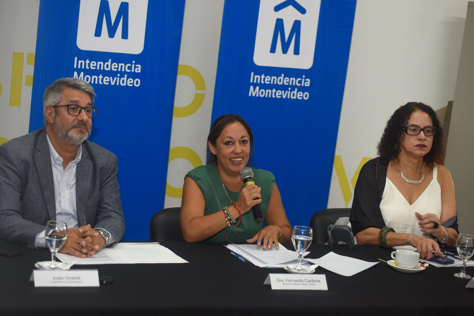 Mesa de autoridades Cardona habla con un micrófono, junto a Onandi y Santos