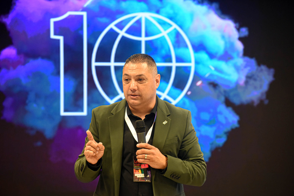 Presidente de la Cámara de Comercio y Negocios LGBT, Adrián Russo Russo habla con un micrófono; detrás, pantalla