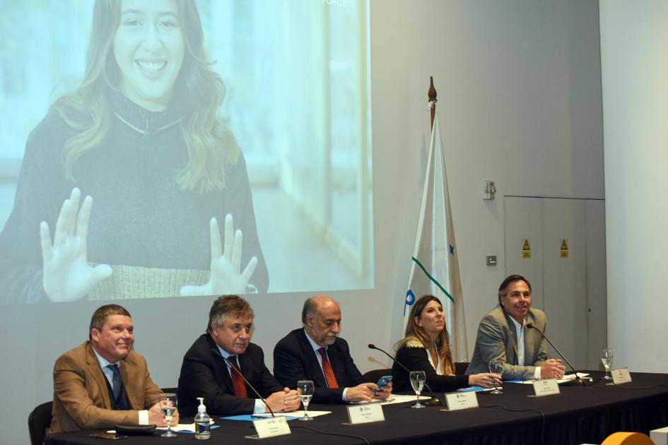 Se escucharon testimonios de participantes del programa en otros países de Latinoamérica Autoridades de la mesa miran hacia arriba; se ve un video de una joven chilena
