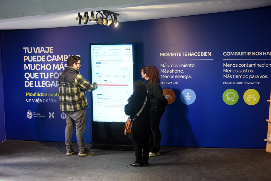 Interior del stand del MIEM Personas observan una pantalla; detrás, pared azul con textos