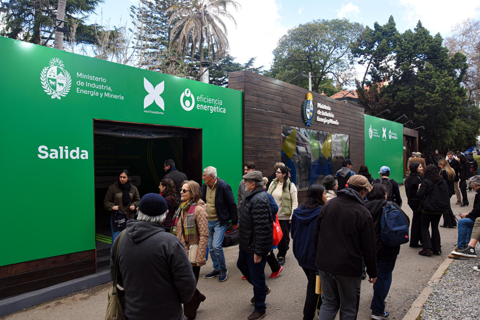 Stand del MIEM, ubicado a metros de la entrada de Av. Lucas Obes, en la Rural del Prado Personas transitan por una calle, frente al stand del MIEM, pintado en verde