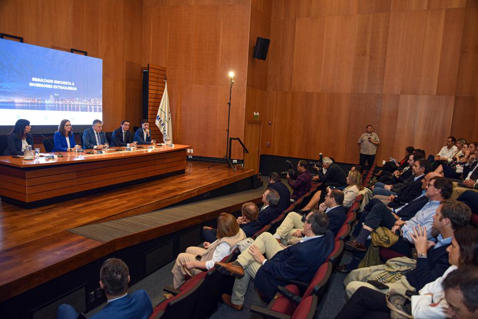 A la izquierda, mesa de autoridades; encima, pantalla; a la derecha, público