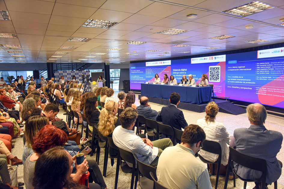 Grupo de personas sentadas observa el panel de autoridades en mesa