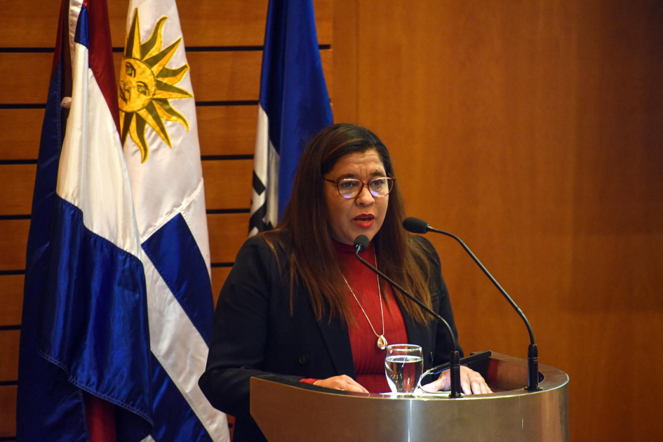 Directora del Programa de Educación Terciaria de UTU, Lorena Guillama Guillama habla en un atril; detrás, pabellones patrios