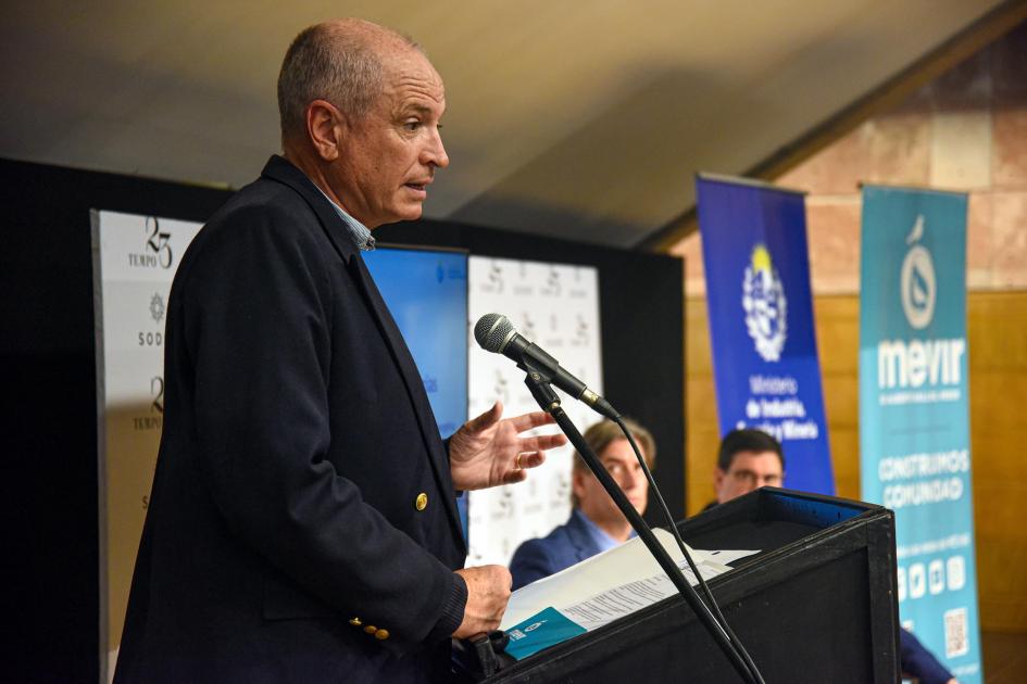 Un hombre habla desde un atril; más lejos se ve a las autoridades y banners de las instituciones