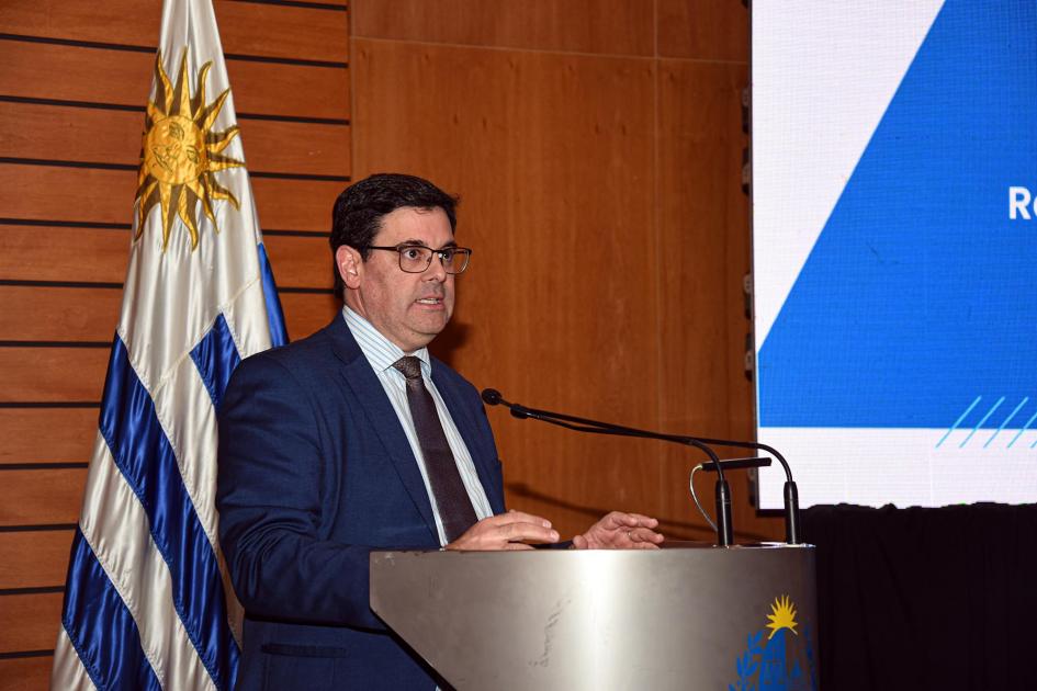 Cantero habla desde un atril; detrás, la bandera uruguaya y un fragmento de una pantalla