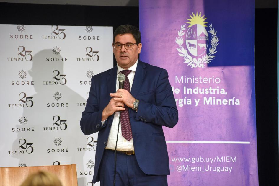 Director nacional de Energía, Fitzgerald Cantero Cantero habla de pie; detrás, banners del MIEM y de MEVIR